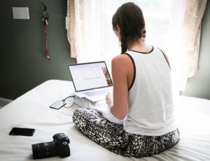 female student with laptop sitting on bed