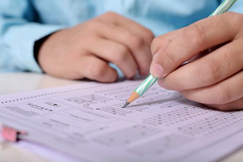 student hand holding pencil on standardized test form