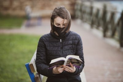 woman on campus wearing mask reading book