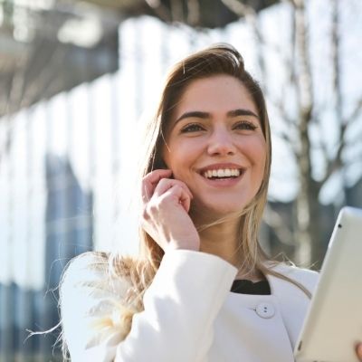 Woman holding tablet while speaking on phone in front of building