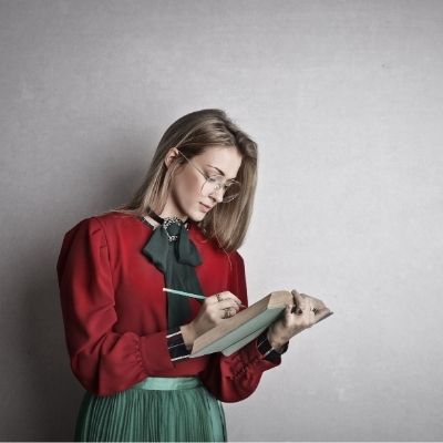 Teacher leaning against wall writing in book