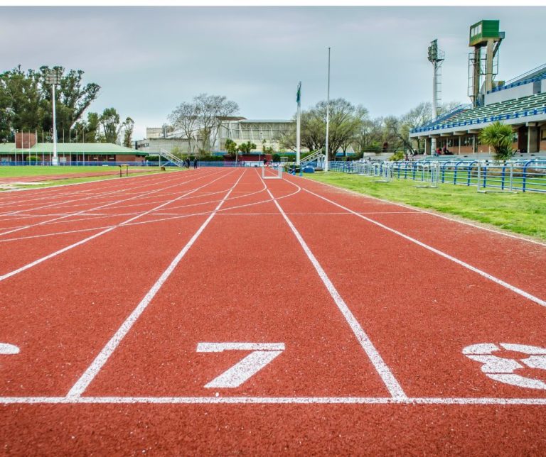 picture of empty track with high school and bleachers in background