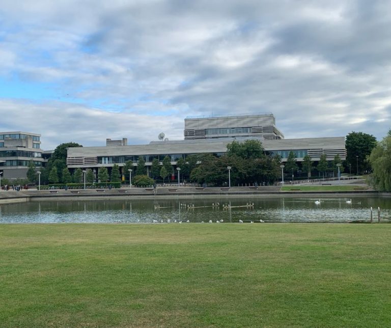 Photo of University College Dublin building taken from across a pond with lawn in foreground