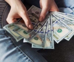 woman's hands holding hundred dollar bills over her lap, wearing jeans