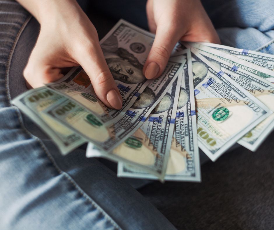 woman's hands holding hundred dollar bills over her lap, wearing jeans