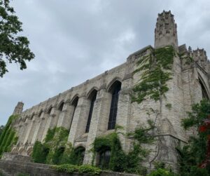 Ivy covered stone building on college campus with cloudy skies