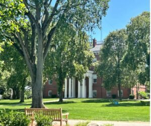 photo of a brick building on Tufts campus with bench and tree in foreground